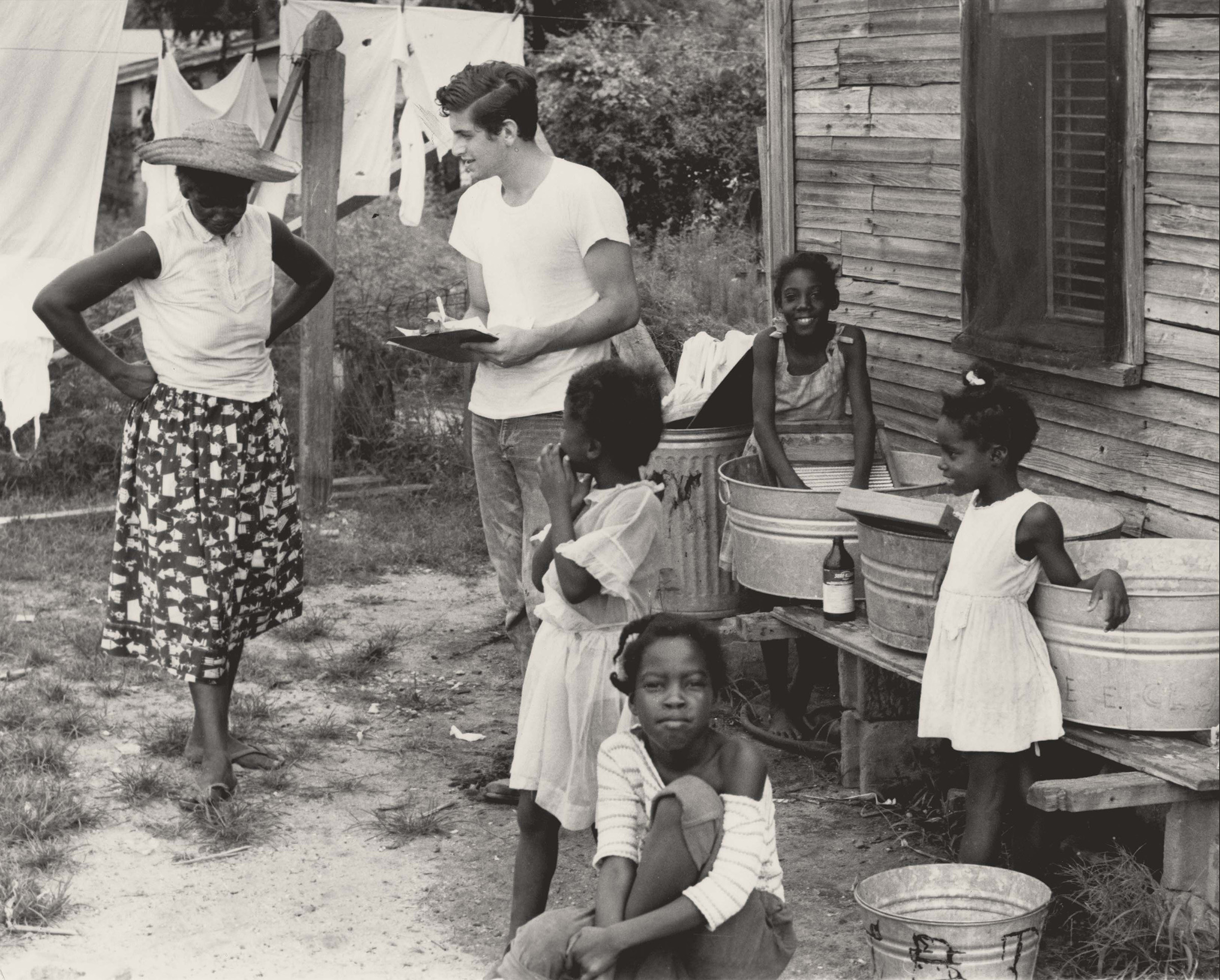 Voter Registration, July 1964. Photograph by Herbert Randall. Volunteer Dick Landerman discusses voter registration procedures with local resident Hattie Mae Pough at her home. The child in the foreground is Trudie Sloan, who lived next door; the other three children are Mrs. Pough's. M351 Herbert Randall Freedom Summer Photographs, Historical Manuscripts, The University of Southern Mississippi.